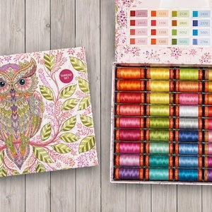 May include: A rectangular Aurifil thread set box featuring a colorful owl illustration on the lid and a grid of forty-eight assorted spools of thread inside. The interior lid displays a color-coded chart with numerical labels for each thread.
