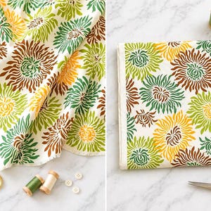 May include: A white fabric featuring a repeating pattern of stylised chrysanthemum flowers in shades of olive green, yellow, and brown. The selvage edge displays the text Freshcut by Heather Bailey - West Webb. Includes gold scissors and spools.
