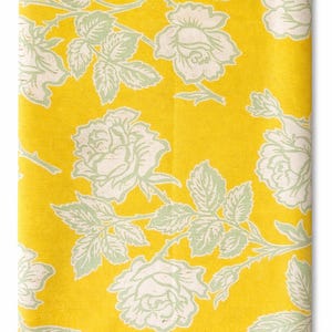 May include: Folded fabric featuring a vibrant yellow backdrop adorned with a repeating pattern of large white roses and pale green leaves. The floral design is a classic, vintage style.