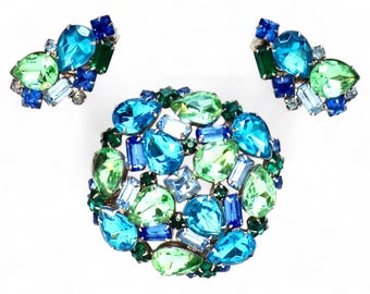May include: A set of blue, green, and light blue rhinestone earrings and a brooch. The brooch is a cluster of rhinestones in a circular shape.