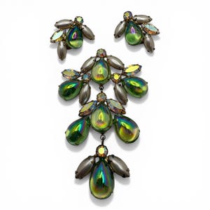 May include: A jewelry set featuring a necklace and matching earrings. The necklace and earrings have iridescent green teardrop-shaped stones with gray accents. The earrings and necklace are set against a white background.