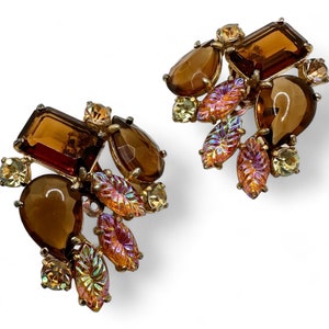 May include: A pair of gold tone clip-on earrings with brown and iridescent stones. The earrings feature a cluster of stones in a leaf-like design.