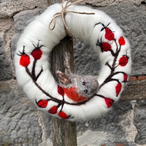 May include: A white felt wreath with a brown felt bird and red felt berries. The wreath is decorated with brown felt branches.