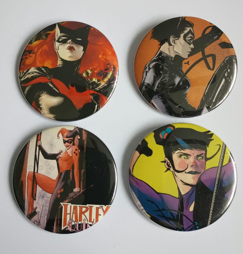May include: Four round buttons featuring comic book characters. The buttons are black with a silver rim. The characters are Harley Quinn, Batgirl, Catwoman, and a character with a purple suit and a yellow background.