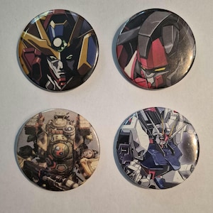 May include: Four circular pin-back buttons featuring detailed illustrations of mecha robots. The top left button shows a dark robot with gold accents, the top right a red and black robot, the bottom left a weathered industrial robot, and the bottom right a white, blue, and red robot.