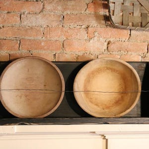 Peut inclure: Deux bols en bois antiques d'aspect rustique et vieilli reposent sur une &eacute;tag&egrave;re noire. Les bols sont ronds, peu profonds et pr&eacute;sentent un grain de bois naturel. L'&eacute;tag&egrave;re est fix&eacute;e contre un mur de briques rouges, cr&eacute;ant une esth&eacute;tique vintage.