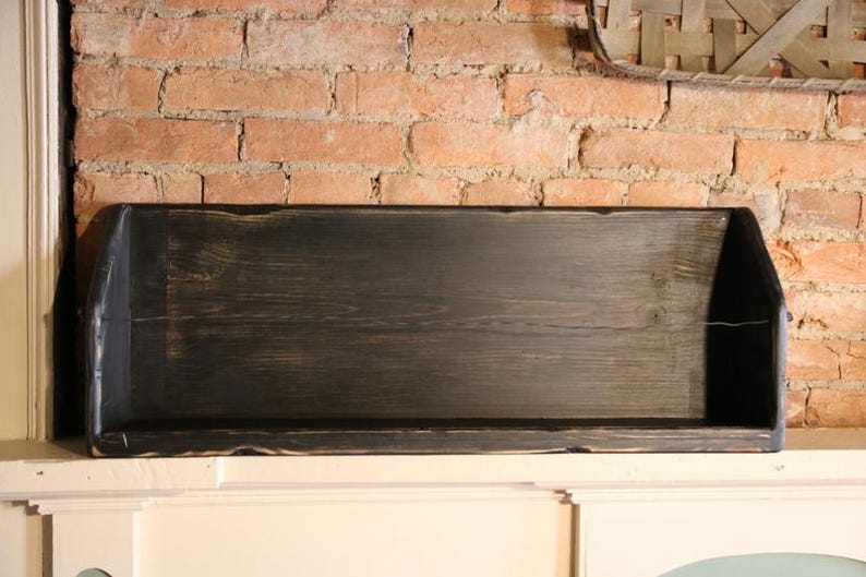 Peut inclure: Une &eacute;tag&egrave;re rectangulaire en bois noir avec une finition vieillie. L'&eacute;tag&egrave;re a un design peu profond avec des c&ocirc;t&eacute;s sur&eacute;lev&eacute;s et est mont&eacute;e contre un mur de briques rouges. L'&eacute;tag&egrave;re mesure environ 76 cm de long.