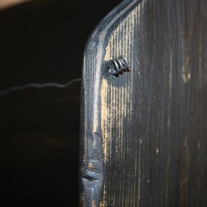 Peut inclure: Gros plan sur une section d'un objet en bois teint&eacute; fonc&eacute;. Le grain du bois est visible, avec une fixation m&eacute;tallique sur le c&ocirc;t&eacute;. L'objet semble faire partie d'un meuble ou d'un &eacute;l&eacute;ment de d&eacute;coration plus grand.