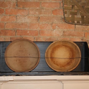 Peut inclure: Deux bols en bois antiques, l'un une assiette et l'autre un bol, sont expos&eacute;s dans une &eacute;tag&egrave;re en bois noir. Les bols sont brun clair avec des accents de fil brun fonc&eacute;, sur un mur de briques rustique.