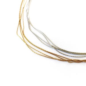 May include: Close-up of several strands of gold and silver metallic ribbon against a white background. The ribbons are thin and slightly twisted, creating a delicate and shimmering effect. The ribbons are likely used for crafting or gift wrapping.