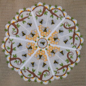 May include: A circular embroidered doily featuring a central bee surrounded by honeycomb patterns, radiating sections with brown tree branches, green leaves, and multiple bees, all bordered by a white daisy chain on a light gray fabric.