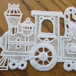 May include: White lace applique of a toy train with a chimney, wheels, and a caboose.