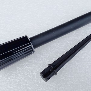 Puede incluir: Una estaca de plástico negro con un extremo puntiagudo y una parte superior roscada. La estaca está diseñada para ser insertada en el suelo para asegurar un objeto.