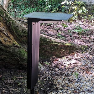 Puede incluir: Una luz solar para exteriores de color negro con un poste rectangular de nervaduras verticales y un panel superior plano y horizontal. La luz cuenta con una fuente de iluminación orientada hacia abajo integrada en la parte inferior del cabezal.