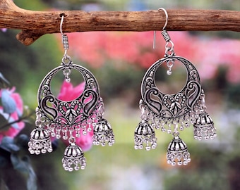 May include: Silver dangle earrings with a circular design and multiple jhumka drops. The earrings feature intricate floral and paisley patterns.