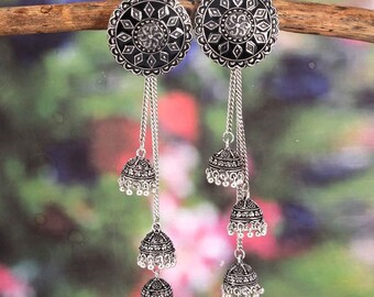 May include: A pair of silver earrings with a round, black, ornate design and three dangling bells.
