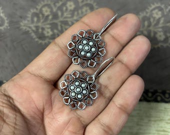 May include: A pair of silver dangle earrings with a floral design and small white beads in the center of each flower.