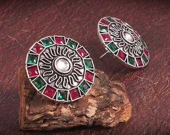 May include: A pair of silver earrings with a circular design. The earrings are decorated with red and green gemstones.