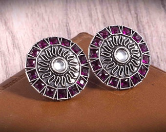 May include: A pair of silver earrings with a circular design. The earrings are decorated with purple gemstones and a silver sunburst pattern.
