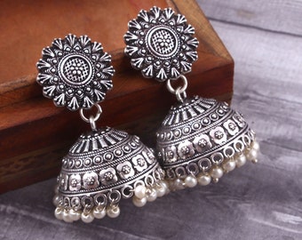 May include: A pair of silver earrings with a floral design and a bell-shaped dangle. The earrings are adorned with small white pearls.