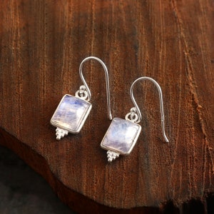 Puede incluir: Un par de pendientes de plata con piedras de luna cuadradas. Los pendientes tienen un diseño sencillo con un pequeño gancho de plata.