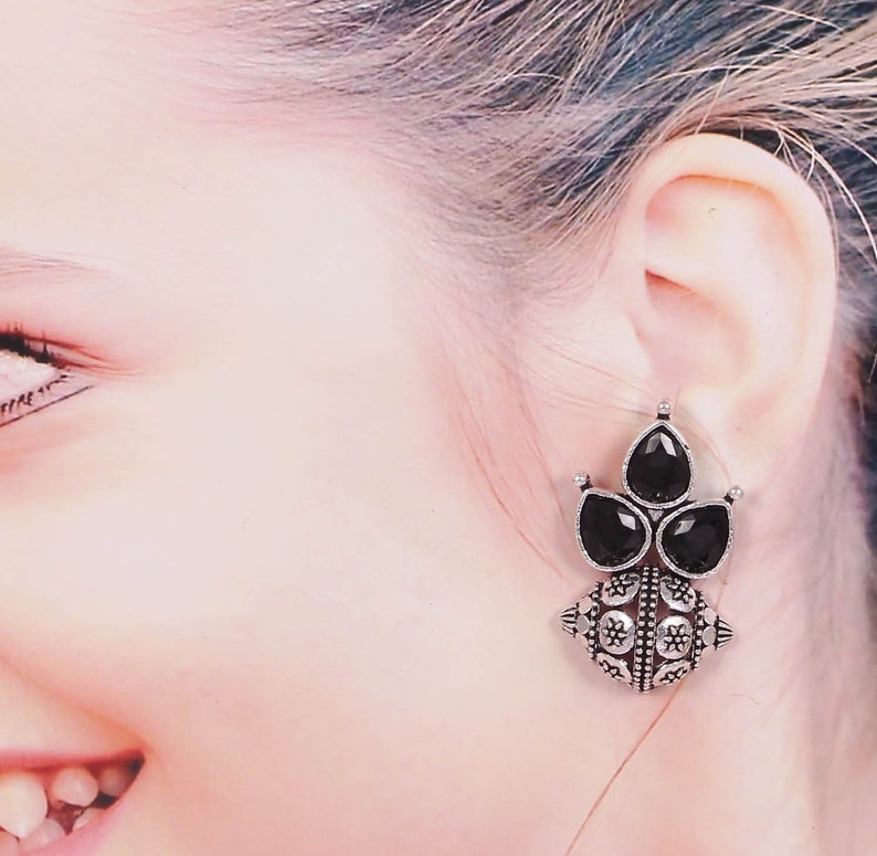 May include: Silver tone earrings with black gemstone accents. The earrings feature a round, ornate design with a cluster of three black gemstones.