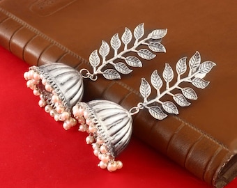 May include: Silver earrings with a leaf design and pearl accents. The earrings are dangling and have a bell-shaped bottom.