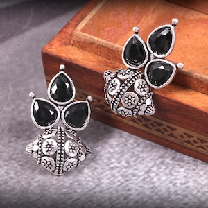 May include: A pair of silver earrings with black gemstone accents. The earrings feature a round, ornate design with a cluster of three teardrop-shaped stones.