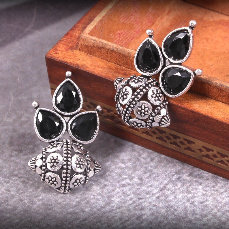 May include: A pair of silver earrings with black gemstone accents. The earrings feature a round, ornate design with a cluster of three teardrop-shaped stones.