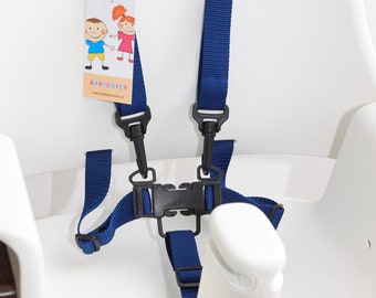 Puede incluir: Un arnés de seguridad azul de cinco puntos con hebillas de plástico negro y correas ajustables fijado a una trona blanca. Una etiqueta rectangular está sujeta a la correa izquierda, con ilustraciones de dos niños y el texto BABYCOVER.