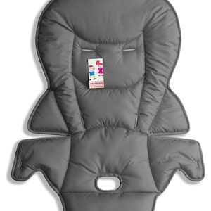 May include: A gray padded baby seat insert with a headrest and arm supports. The insert has a central opening and a tag with cartoon figures. The material appears soft and quilted, designed for comfort and support.
