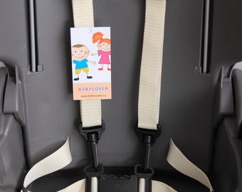 Puede incluir: Un asiento de trona de plástico gris con un sistema de arnés de cinco puntos con correas de nailon color hueso y hebillas de plástico negro. Una etiqueta rectangular con dibujos animados y el texto BABYCOVER está unida a la correa izquierda.