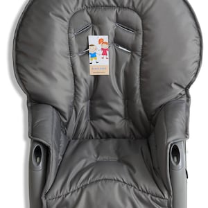 May include: A gray baby high chair cover with a quilted design. The cover has a padded headrest and armrests. A tag with the text "BABYCOVER" and a website address is attached to the cover.