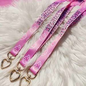 Op de afbeelding: Drie roze lanyards met gouden hartvormige sluitingen. Elke lanyard heeft een wit wolkendesign en de tekst "HIGHKIDS" erop gedrukt.