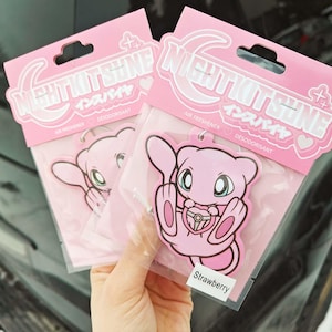 Op de afbeelding: Twee roze luchtverfrissers met een cartoon karakter ontwerp. De verpakking leest "NIGHTKITSUNE" in witte letters met Japanse karakters. De luchtverfrissers zijn aardbei geurig.