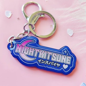 Könnte beinhalten: Ein blauer und rosa Acryl-Schlüsselanhänger mit dem Text "NIGHTKITSUNE" und dem japanischen Text "インスバイア" mit einem rosa Herz.