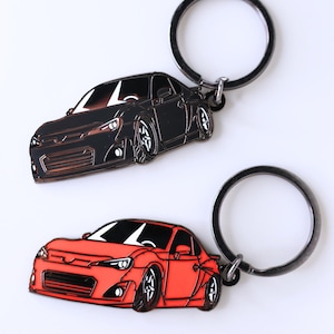 Peut inclure: Deux porte-clés en métal représentant une voiture noire et une voiture rouge. Les porte-clés sont en forme de voiture de sport avec un design détaillé.