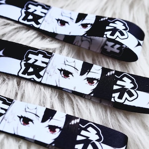 May include: Black and white patterned ribbon featuring anime-style eyes with red irises and Japanese text. The ribbon is displayed on a fluffy white surface. The design repeats along the length of the ribbon.