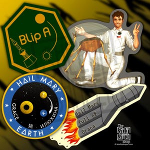 Op de afbeelding: Een verzameling kleurrijke stickers met ruimte-thema ontwerpen. Eén sticker toont een raket met de tekst "Blip A". Een andere toont een astronaut en een Mars-drietand. Andere stickers bevatten de tekst "Hail Mary" en "Grace Earth."