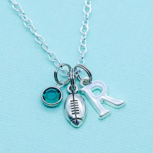 May include: Silver necklace with a green gemstone, a football charm, and a letter R charm.