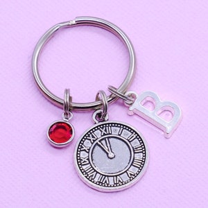 May include: Silver key ring with a red jewel, a clock face charm, and a letter "B" charm.