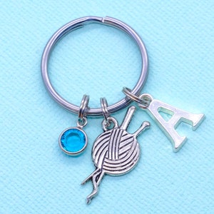 May include: Silver keyring with a blue crystal charm, a ball of yarn charm, and a letter A charm.