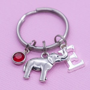 May include: Silver keyring with a red rhinestone charm, a silver elephant charm, and a silver charm with the letter E.