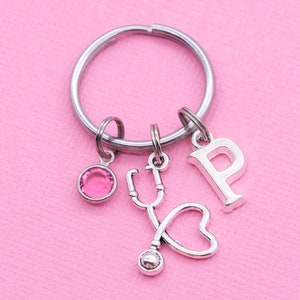 May include: Silver keychain with a pink crystal charm, a stethoscope charm with a heart, and a letter 'P' charm.