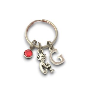May include: A silver keyring with a red crystal charm, a small silver gnome charm, and a silver charm with the letter G.