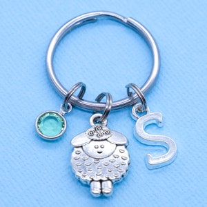 May include: Silver keyring with a green crystal charm, a silver sheep charm, and a silver letter 'S' charm.
