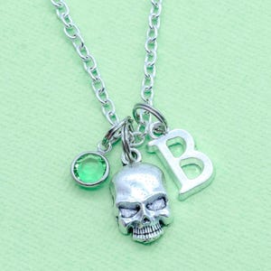 May include: A silver necklace with a skull charm, a green crystal charm, and a letter 'B' charm.
