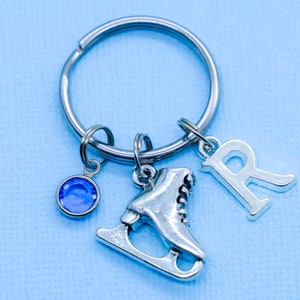 May include: Silver key chain with a blue crystal charm, a silver ice skate charm, and a silver charm with the letter R.
