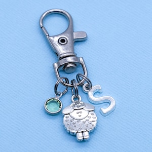 May include: Silver keyring with a charm of a sheep, a green crystal, and the letter 'S'.