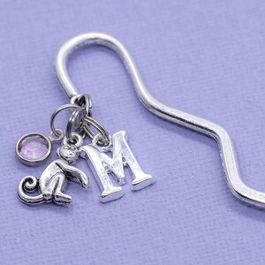 May include: Silver bookmark with a pink crystal charm, a monkey charm, and a letter M charm.